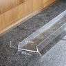 Clear PVC plinth sealing strip installed at the bottom of a wooden kitchen cabinet plinth to block water and dirt, dimensions shown.